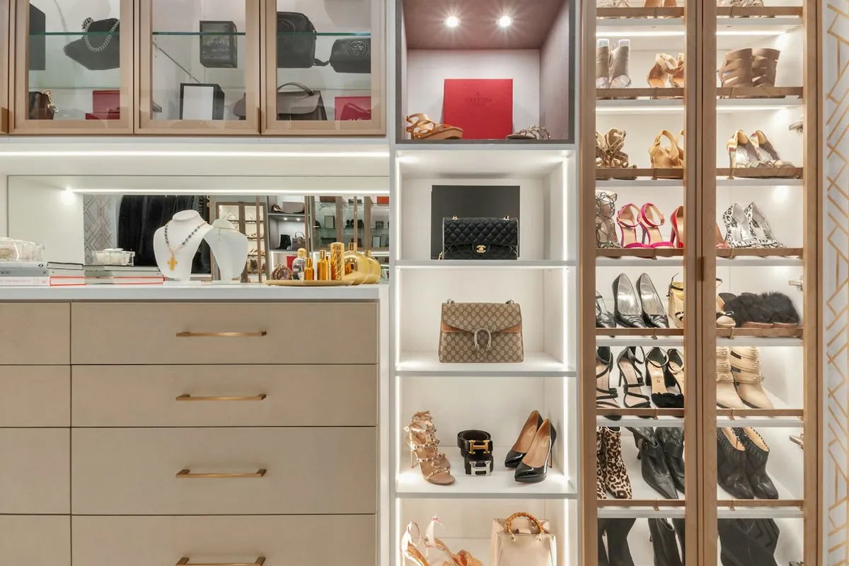 A custom walk-in closet with glass fronted cabinets, drawers and lit shoe shelving in a Mobile AL home